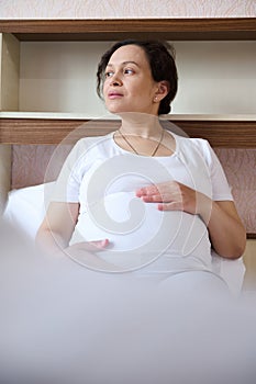 Close-up pregnant woman sitting on bed, stroking her big belly, enjoying pregnancy and contact with her future child