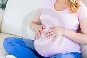 Close up of pregnant woman sitting on couch touching her belly