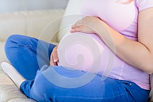 Close up of pregnant woman sitting on couch touching her belly