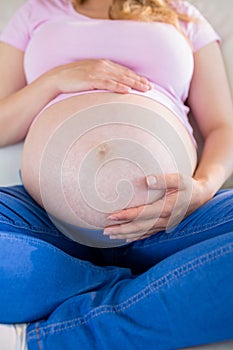 Close up of pregnant woman sitting on couch touching her belly