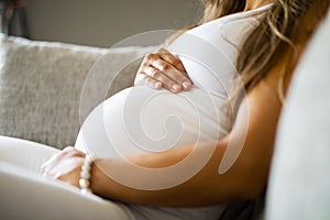 Close-up of pregnant woman sitting in sofa with her hands at belly