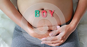Close up Pregnant woman sitting on soft sofa and touching her belly with sign BOY in front of her belly