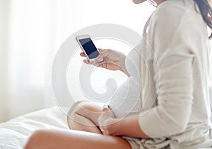 Close up of pregnant woman with smartphone in bed