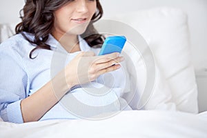 Close up of pregnant woman with smartphone in bed