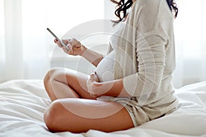 Close up of pregnant woman with smartphone in bed