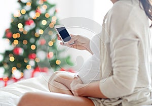 Close up of pregnant woman with smartphone in bed