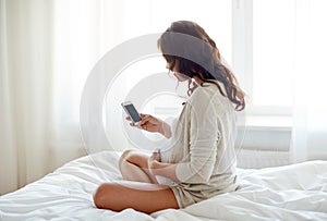 Close up of pregnant woman with smartphone in bed