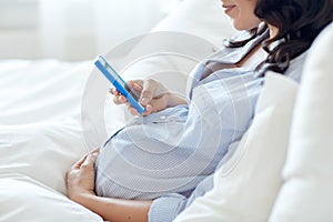 Close up of pregnant woman with smartphone in bed