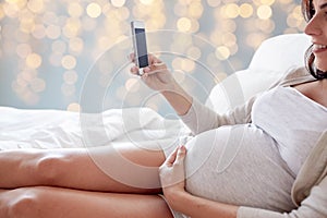 Close up of pregnant woman with smartphone in bed