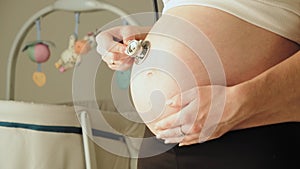 Close-up of a pregnant woman with stethoscope listening baby heartbeats in her belly.