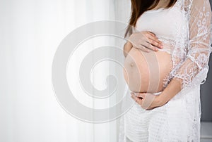 Close up of pregnant woman stroking belly on window background