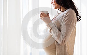 Close up of pregnant woman with tea cup at window