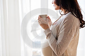 Close up of pregnant woman with tea cup at window