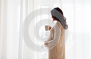 Close up of pregnant woman with tea cup at window