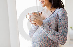 Close up of pregnant woman with tea cup at window