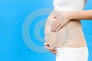 Close up of pregnant woman in underwear with supporting bandage against backache at blue background with copy space. Orthopedic