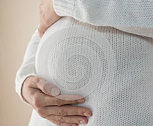 Close-up of a pregnant woman in a white sweater stroking her pregnant belly. Image of pregnancy and expectation of a