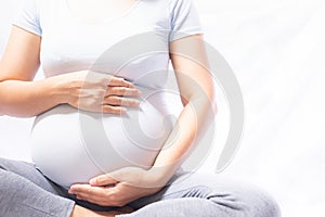 Close up pregnant women sitting and touching her belly with hands on white background