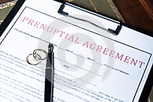 Close-up of a prenuptial agreement form with wedding rings and a fountain pen, indicating the legal aspects of marriage