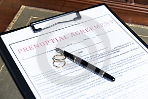 Close-up of a prenuptial agreement form with wedding rings and a fountain pen, indicating the legal aspects of marriage