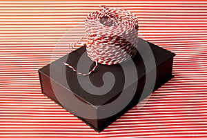 Close-up of present. Black box, resent packaging paper with red and white stripes and striped cord.