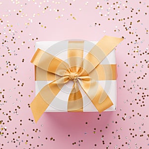 Close up of present box in gold ribbon on pink background