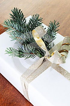 Close-up of present on a wooden vintage table. White gift box with golden bow and branch of Christmas tree.