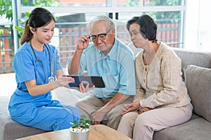 Close up pretty Asian nurse or doctor sit on sofa and use tablet to give suggestion or consult data to couple senior man and woman