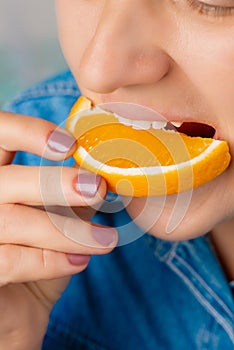 Close-up of a pretty Caucasian woman biting an orange slice. Front three-quarter view. High angle view. Indoors