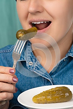 Close-up of a pretty Caucasian woman holding a fork and a plate with pickled cucumber. Front three-quarter view. Low angle view.