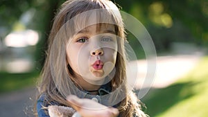 Close-up pretty little girl gesturing air kiss in slow motion looking at camera. Front view headshot of cute Caucasian