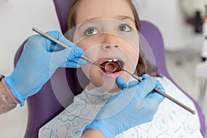 Close-up of pretty little girl opening his mouth wide during treating her teeth by the dentist