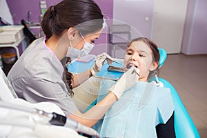 Close-up of pretty little girl opening his mouth wide during treating her teeth by the dentist