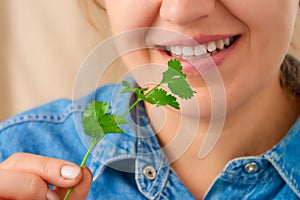 Close-up of a pretty smiling Caucasian woman holding a green sprig of fresh celery in her hand. Front view from low angle