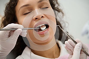 Close-up of pretty woman, patient in dentistry clinic, with closed eyes and open mouth while hygienist dentist examining her teeth