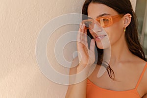 Close-up of pretty young caucasian woman looking at distance corrects sunglasses during day.