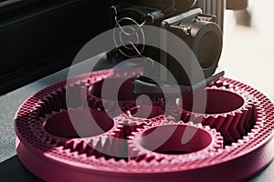 Close up on print head of 3D-printer making a planetary gear part from pink plastic.