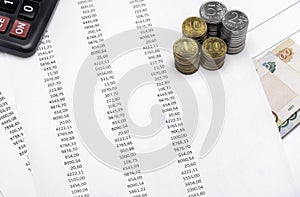 Close-up printed numbers on white paper, on which lies the calculator, coins of different values of rubles and next to paper bills