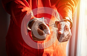 Close up of prisoner`s hands with handcuffs in orange jumpsuit at prison