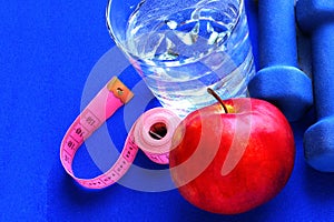 Close up of a pristine red apple two dumbbells and glass water