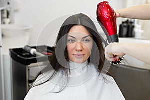 Close-up of the process of hair styling in a beauty salon with a hair dryer and a comb. The hairdresser dries the girls