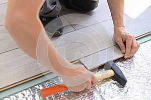 Close up process of laying laminate. Man with hammer installing new laminated wooden floor, top view