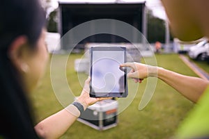 Close Up Of Production Team Looking At Digital Tablet Setting Up Outdoor Stage For Music Festival 