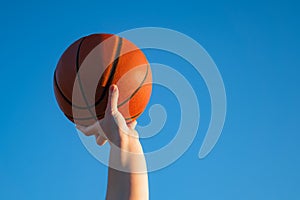 Close up of professional basketball player holding a ball in the hand. Street basketball athlete with a ball and blue sky in the