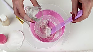Close up of Professional beautician makes a white clay mask, she mixes it a pink bowl