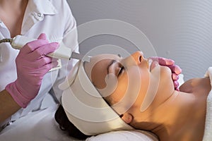 Close-up, professional beautician using an ultrasonic facial cleanser, cleans the skin of a girl patient, in a beauty salon