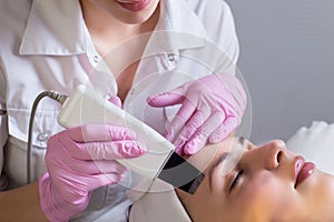 Close-up, professional beautician using an ultrasonic facial cleanser, cleans the skin of a girl patient, in a beauty salon