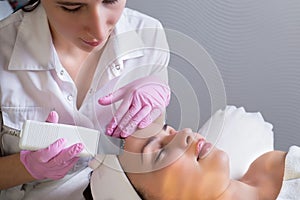 Close-up, professional beautician using an ultrasonic facial cleanser, cleans the skin of a girl patient, in a beauty salon