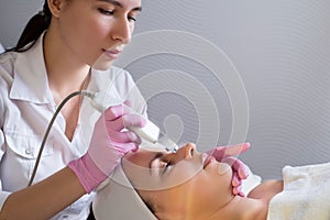 Close-up, professional beautician using an ultrasonic facial cleanser, cleans the skin of a girl patient, in a beauty salon