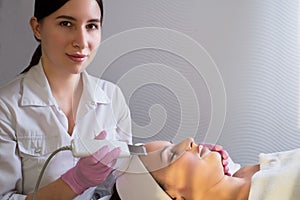 Close-up, professional beautician using an ultrasonic facial cleanser, cleans the skin of a girl patient, in a beauty salon